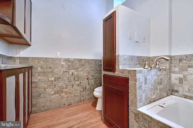 bathroom featuring tile walls, wood-type flooring, toilet, and a bath