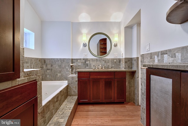 bathroom with tiled bath, wood-type flooring, vanity, and tile walls