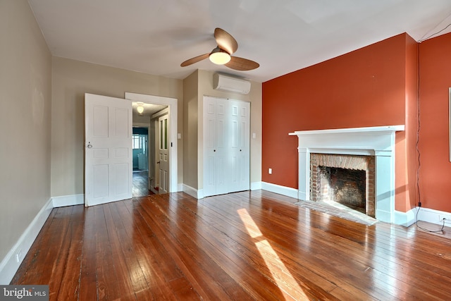 unfurnished living room featuring a brick fireplace, an AC wall unit, hardwood / wood-style flooring, and ceiling fan