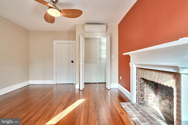 unfurnished living room featuring a brick fireplace, a wall unit AC, wood-type flooring, and ceiling fan