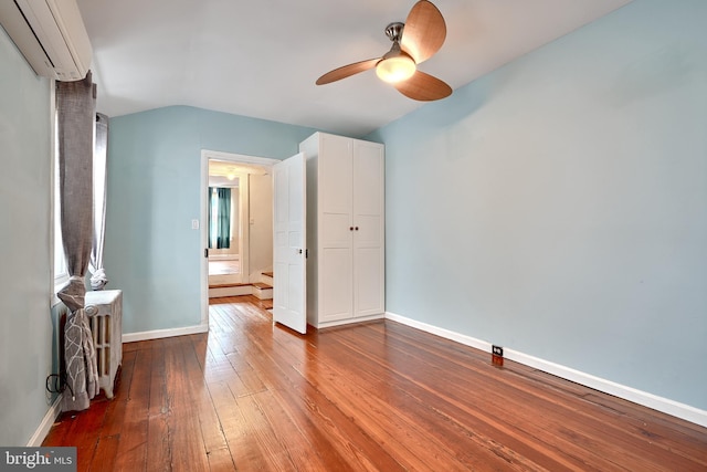 unfurnished bedroom with a wall unit AC, ceiling fan, lofted ceiling, and hardwood / wood-style flooring