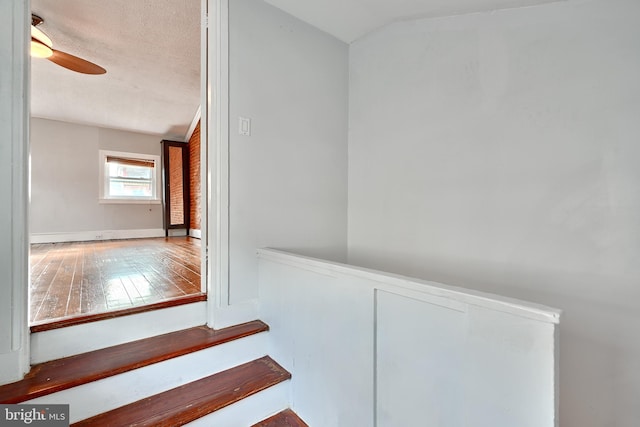 stairs featuring ceiling fan, wood-type flooring, a textured ceiling, and vaulted ceiling