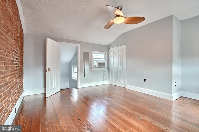 spare room featuring brick wall, hardwood / wood-style flooring, ceiling fan, and vaulted ceiling