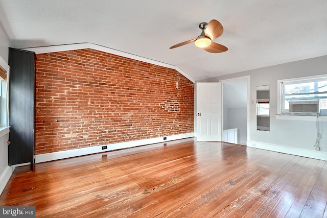 unfurnished living room with cooling unit, hardwood / wood-style flooring, lofted ceiling, ceiling fan, and brick wall