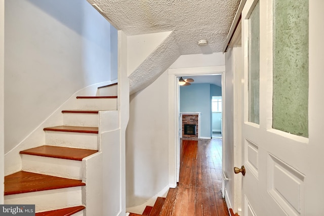 stairs with hardwood / wood-style floors, a textured ceiling, vaulted ceiling, and a brick fireplace