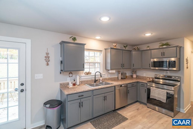 kitchen with gray cabinets, light wood-type flooring, appliances with stainless steel finishes, and sink