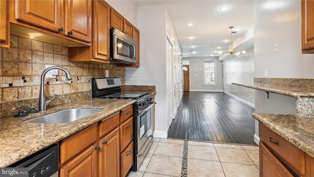 kitchen with stainless steel appliances, a notable chandelier, sink, light stone countertops, and light hardwood / wood-style flooring