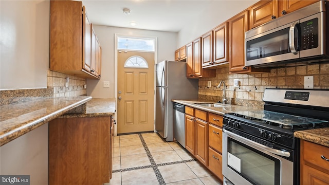 kitchen with sink, tasteful backsplash, light tile patterned flooring, appliances with stainless steel finishes, and dark stone countertops