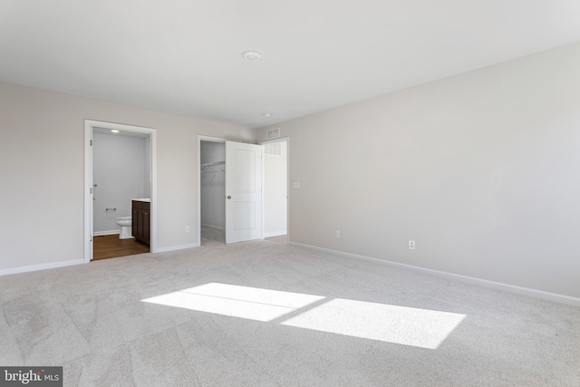 unfurnished bedroom featuring ensuite bath, light carpet, a walk in closet, and a closet