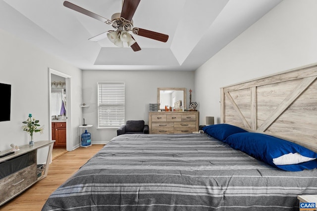 bedroom with hardwood / wood-style flooring, ceiling fan, ensuite bath, and a tray ceiling