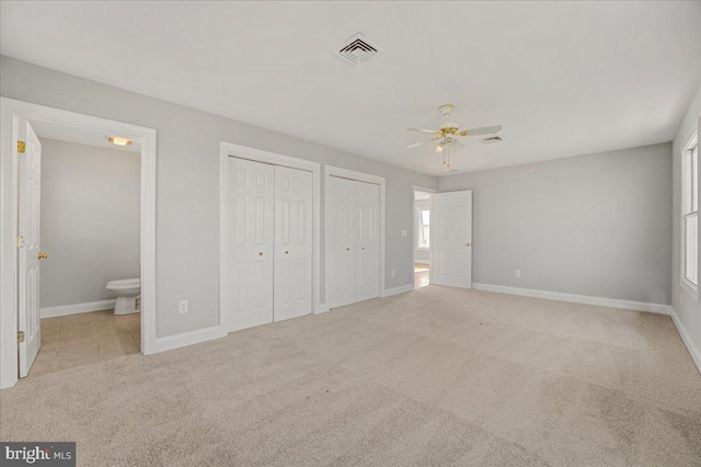 unfurnished bedroom featuring ceiling fan, light colored carpet, connected bathroom, and two closets