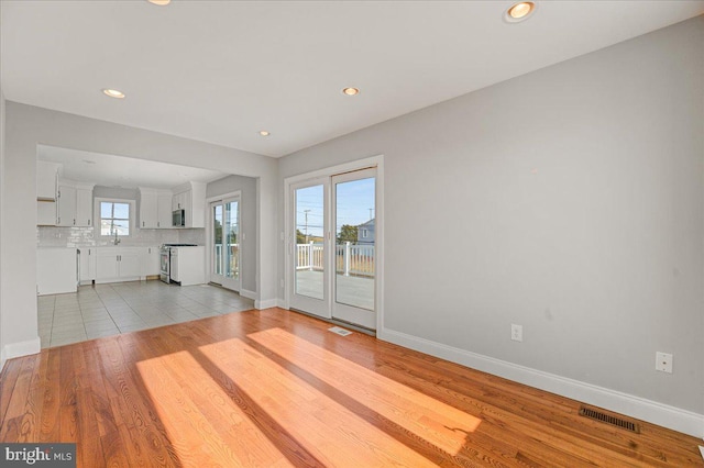 unfurnished living room featuring a healthy amount of sunlight, light wood-type flooring, and sink