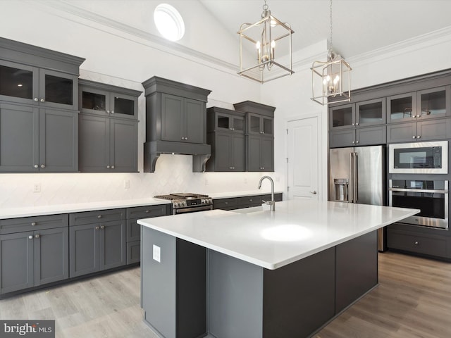 kitchen with premium appliances, light wood-type flooring, an island with sink, and decorative light fixtures