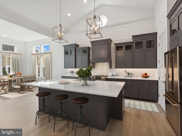 kitchen featuring a center island with sink, hanging light fixtures, appliances with stainless steel finishes, light hardwood / wood-style floors, and dark brown cabinetry