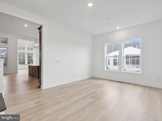 unfurnished room with plenty of natural light, light hardwood / wood-style floors, and an inviting chandelier