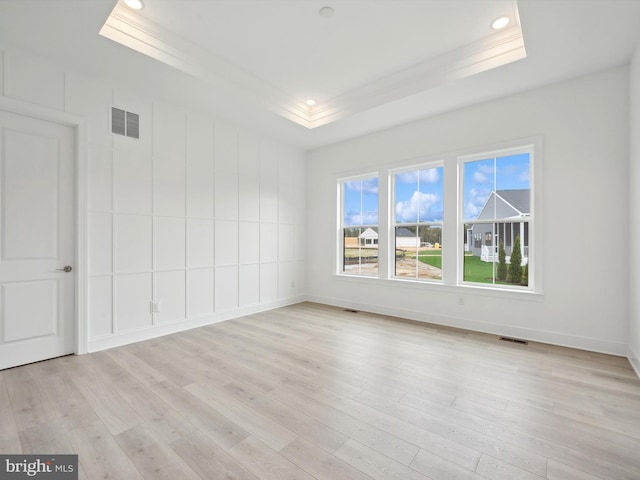 empty room with light wood-type flooring and a tray ceiling