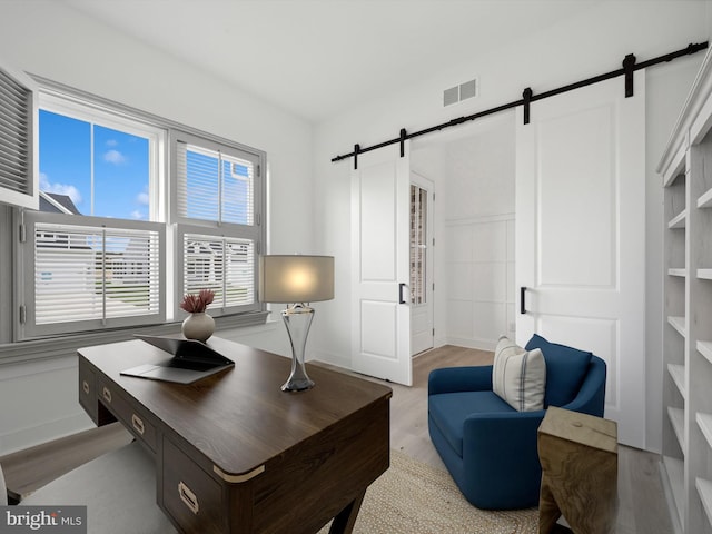 office space with built in shelves, a barn door, and light hardwood / wood-style flooring