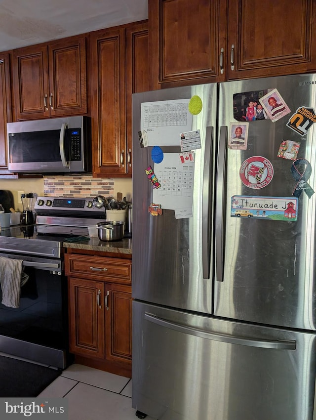 kitchen with decorative backsplash, stainless steel appliances, light tile patterned floors, and dark stone countertops