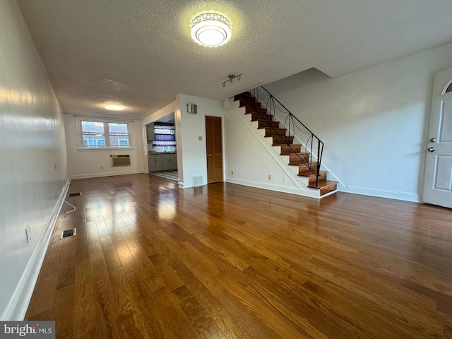 unfurnished living room with an AC wall unit, dark wood-type flooring, and a textured ceiling