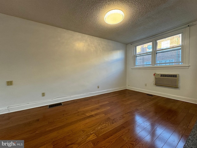 empty room featuring dark hardwood / wood-style floors, a textured ceiling, and an AC wall unit