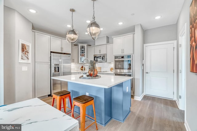 kitchen with appliances with stainless steel finishes, a kitchen bar, decorative light fixtures, a center island, and light wood-type flooring