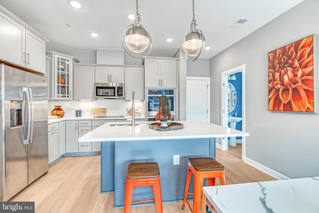 kitchen with white cabinetry, light wood-type flooring, appliances with stainless steel finishes, backsplash, and hanging light fixtures