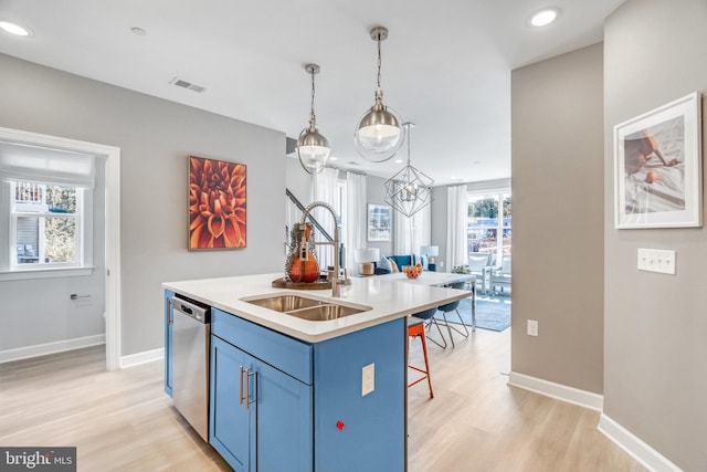 kitchen featuring a center island with sink, sink, stainless steel dishwasher, hanging light fixtures, and light hardwood / wood-style flooring