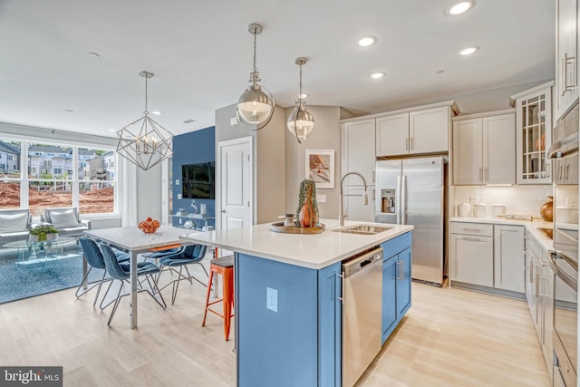 kitchen with a kitchen island with sink, light wood-type flooring, appliances with stainless steel finishes, and hanging light fixtures