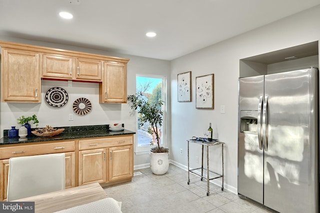 kitchen with stainless steel refrigerator with ice dispenser, light tile patterned floors, and dark stone countertops