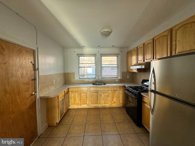 kitchen with gas stove, stainless steel refrigerator, light tile patterned floors, decorative backsplash, and sink