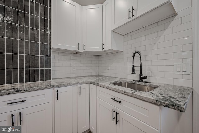 kitchen with tasteful backsplash, sink, light stone counters, and white cabinets