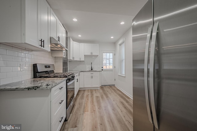 kitchen with tasteful backsplash, white cabinetry, appliances with stainless steel finishes, light stone countertops, and light hardwood / wood-style floors