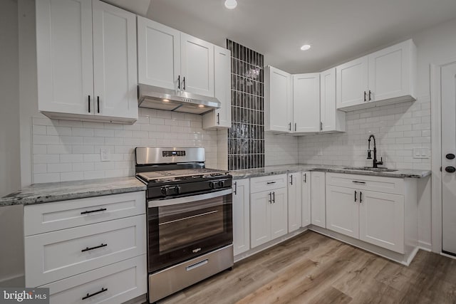 kitchen with stainless steel range with gas cooktop, sink, tasteful backsplash, light hardwood / wood-style flooring, and white cabinets