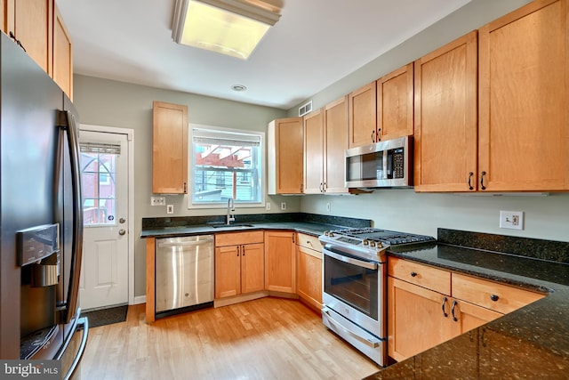 kitchen featuring dark stone counters, sink, light hardwood / wood-style floors, and stainless steel appliances