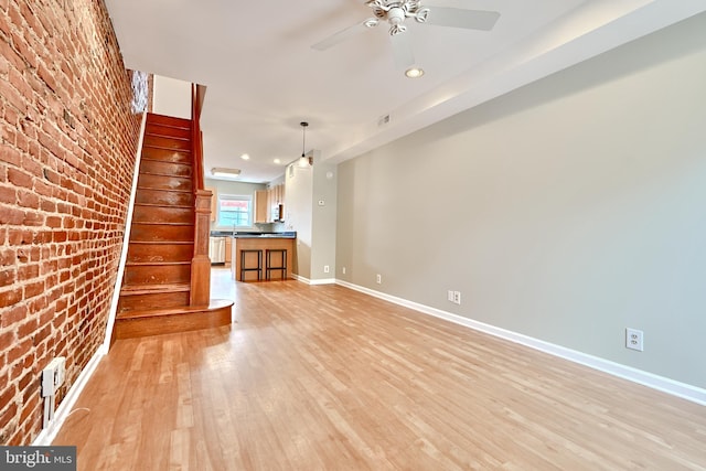 unfurnished living room featuring ceiling fan, light hardwood / wood-style floors, and brick wall