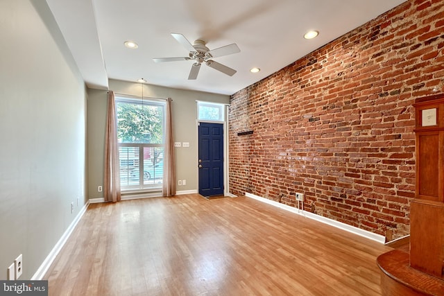 empty room with ceiling fan, brick wall, and light hardwood / wood-style flooring