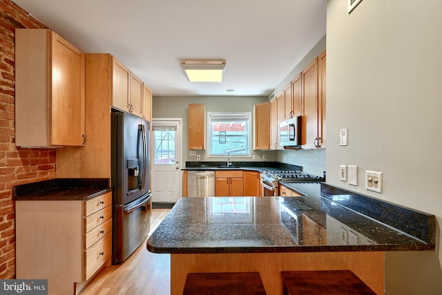 kitchen with stainless steel appliances, light hardwood / wood-style floors, sink, kitchen peninsula, and dark stone countertops