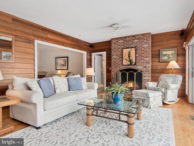 living room featuring a brick fireplace, wood walls, ceiling fan, and hardwood / wood-style flooring