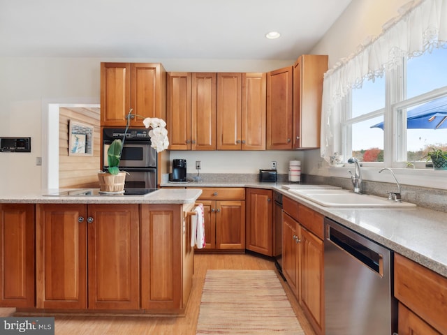 kitchen with black appliances, light stone counters, sink, and light hardwood / wood-style flooring