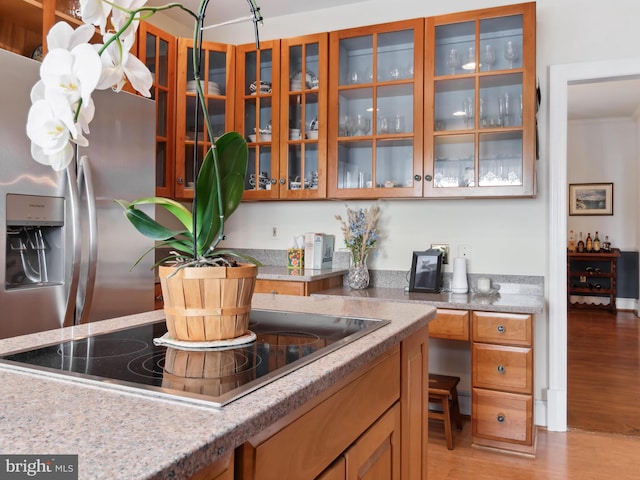 kitchen with stainless steel fridge, light stone counters, black electric cooktop, and light hardwood / wood-style flooring