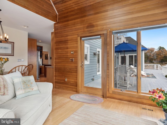 living room featuring light hardwood / wood-style flooring, wooden ceiling, a notable chandelier, lofted ceiling, and wood walls