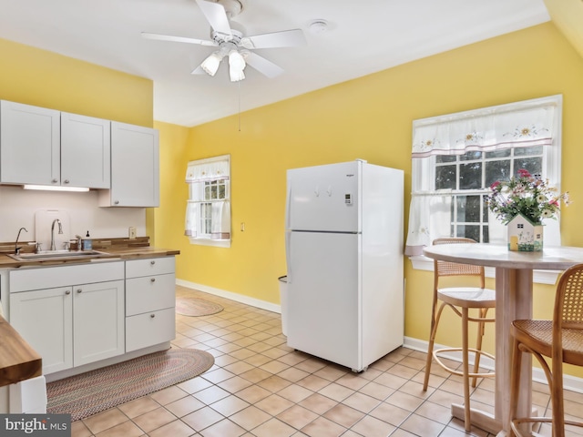 kitchen with white cabinetry, sink, ceiling fan, white refrigerator, and light tile patterned flooring