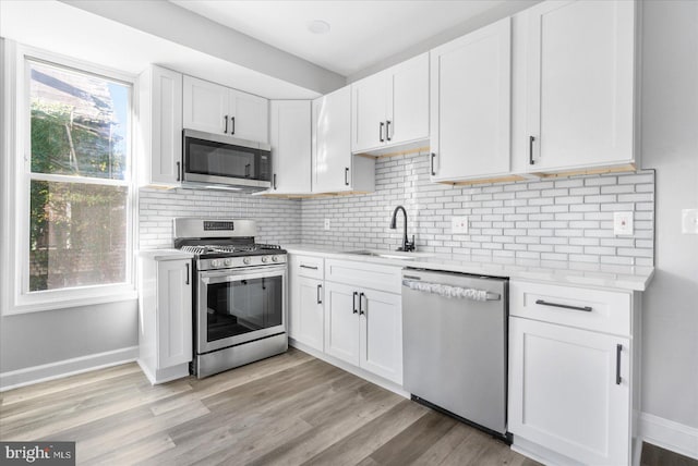 kitchen with stainless steel appliances, white cabinets, sink, and light hardwood / wood-style flooring