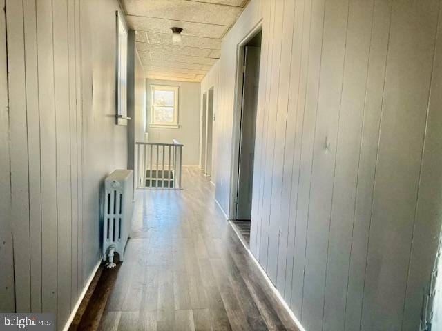 corridor with dark hardwood / wood-style flooring, wood walls, and radiator heating unit