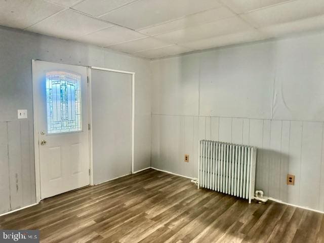 foyer entrance with dark wood-type flooring, radiator, and wood walls