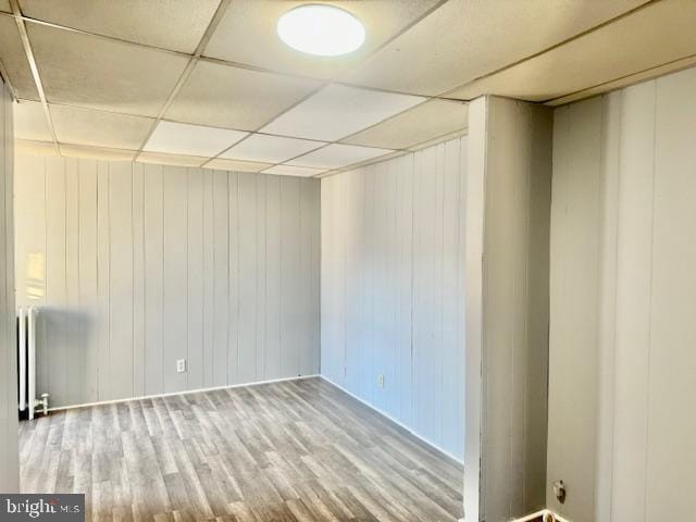 spare room with wood walls, a paneled ceiling, radiator heating unit, and hardwood / wood-style floors