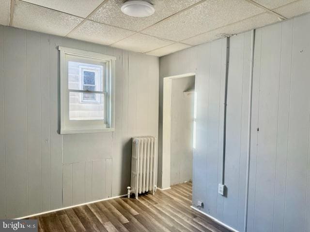 unfurnished bedroom with wood walls, hardwood / wood-style flooring, radiator heating unit, and a drop ceiling