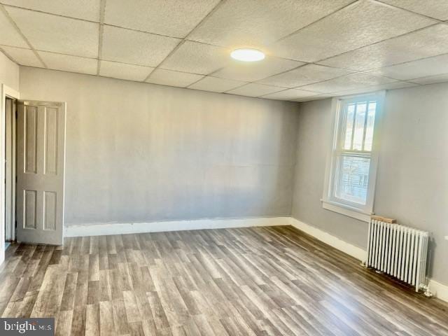 unfurnished room with a drop ceiling, radiator heating unit, and wood-type flooring