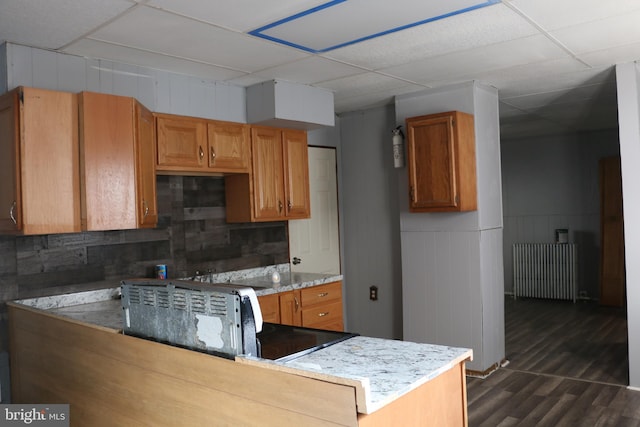 kitchen with a drop ceiling, dark hardwood / wood-style flooring, light stone counters, kitchen peninsula, and tasteful backsplash