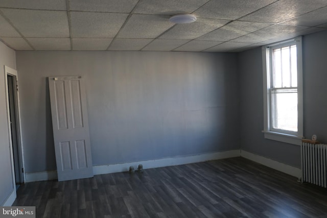 unfurnished room with a drop ceiling, a wealth of natural light, dark wood-type flooring, and radiator heating unit